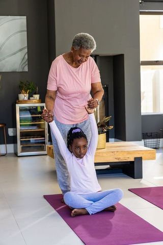 African grandmother guiding granddaughter stretching during at-home yoga session