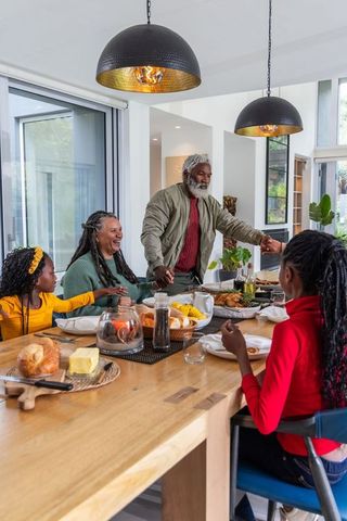 Multigenerational african american family holding hands sharing cozy roasted chicken dinner