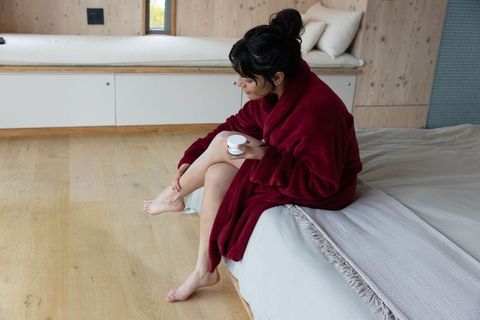 Minimalist Serenity: Asian Woman Applying Lotion in Cozy Bedroom
