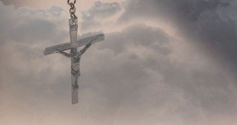 Silver crucifix pendant floating above cloudy sky with soft halo and ample copy space