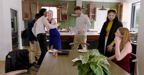 Multicultural friends celebrating in modern kitchen in formal wear, hugging and laughing