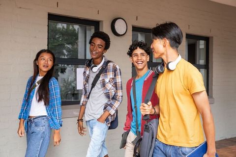 Diverse Teens Walking and Chatting on Campus Wearing Headphones and Carrying Backpacks