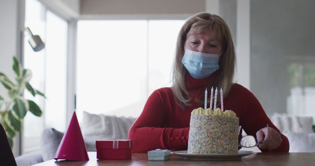 Senior woman celebrating birthday alone with face mask and cake - Download Free Stock Photos Pikwizard.com