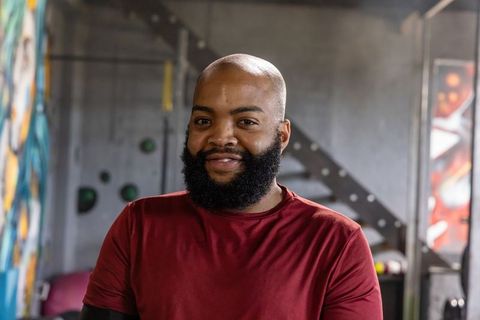 Smiling african man standing in urban gym wearing maroon top, concrete interior portrait