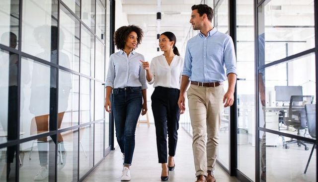 Multicultural team walking and exchanging ideas in modern glass office corridor