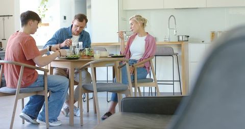 Family enjoying healthy meal around wooden dining table in sunlit open-plan modern kitchen