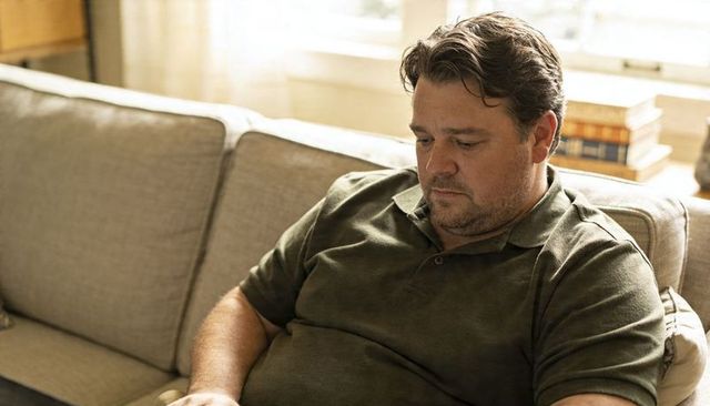 Contemplating middle-aged man sitting on beige sofa gazing downward in warm daylight
