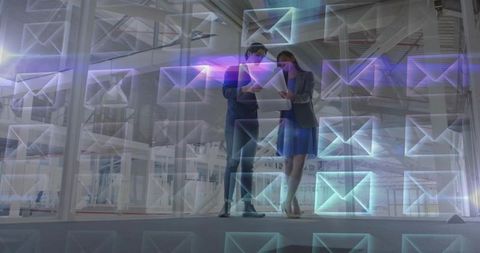 Colleagues examining tablet in industrial office with holographic email icons overlay