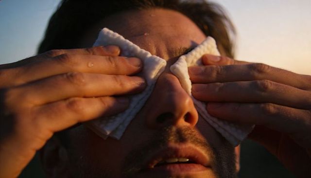 Man pressing damp cotton pads over closed eyes during golden hour for soothing relief