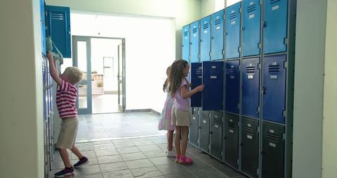 Elementary students opening lockers in bright school hallway preparing backpacks and books