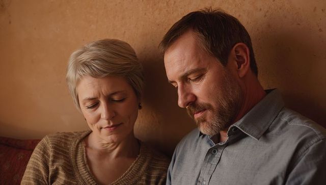 Mature couple leaning together on sofa sharing quiet reflective moment in warm cozy interior