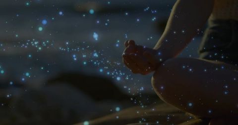 Coastal dusk meditation with glowing bioluminescent particles, serene cross-legged pose
