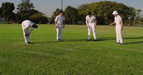 Sunlit cricket players standing and strategizing on green field in white uniforms