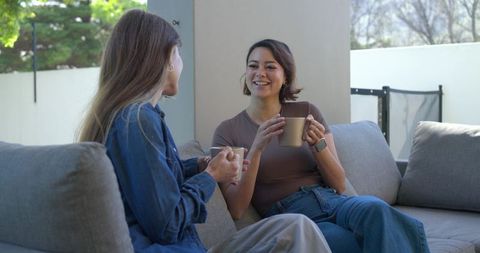Friends enjoying coffee on covered patio sofa sharing relaxed conversation and laughter
