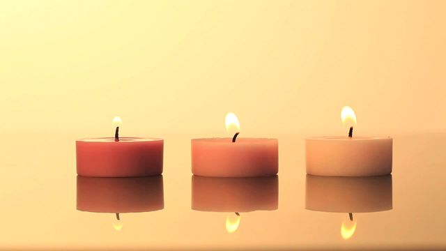 Three lighted candles creating a tranquil atmosphere with a warm yellow background. Ideal for spa and wellness promotions, meditation and relaxation articles, or introducing aromatherapy products. The calm glow of the candles adds a serene and peaceful touch.