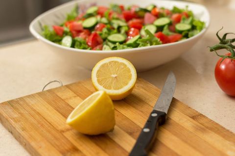 Lemon halves sitting on wooden cutting board with fresh garden salad and chef knife