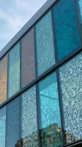 Vertical video tilting over patterned glass facade with colorful reflections and skyline