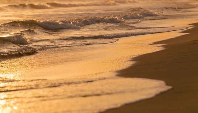 Golden sunset waves lapping sandy shoreline creating reflective bands of wet sand
