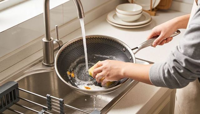 Woman washing nonstick pan with yellow sponge at stainless steel kitchen sink