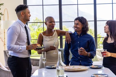Multiethnic friends chatting over cocktails at modern kitchen island during daytime party