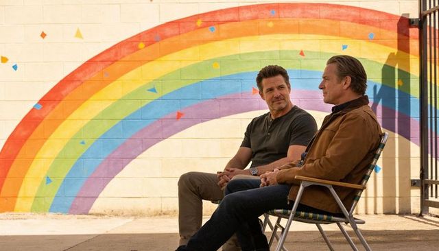 Middle-aged men sitting and talking by rainbow mural, casual outdoor urban friendship