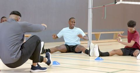 Diverse male teammates stretching and smiling on indoor court during team warmup