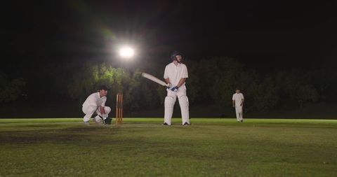 Night cricket match under floodlights showing batsman at crease with wicketkeeper