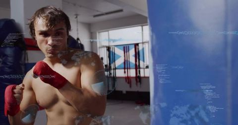 Male boxer training with red hand wraps punching heavy bag with futuristic hud overlays