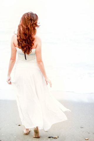 Serene Woman with Red Hair in White Dress Strolling on Beach