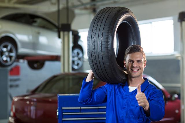Portrait of mechanic carrying a tyre in repair garage