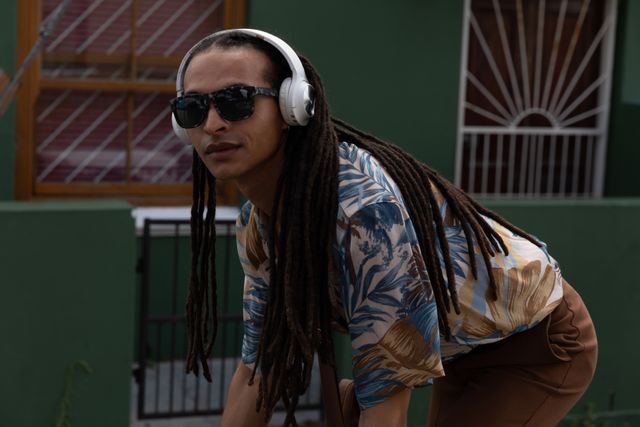 Biracial alternative man with dreadlocks, sunglasses and headphones out and about in the city on a sunny day, riding bike. Urban trendy man on the go.