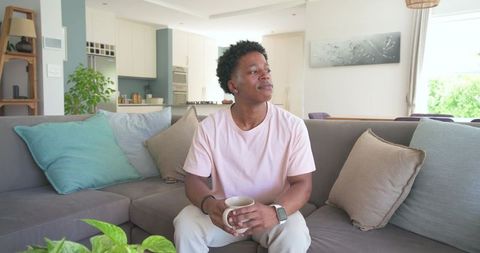 African american man relaxing on sofa holding mug in modern open-plan living room