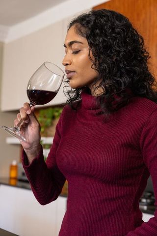Elegant Woman Savoring and Scenting Red Wine in Modern Kitchen