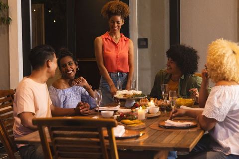 Diverse friends gathering around candlelit dinner table, host presenting cupcake stand