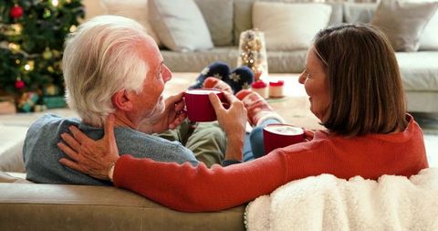 Senior Couple Enjoying Cocoa by Christmas Tree in Cozy Living Room