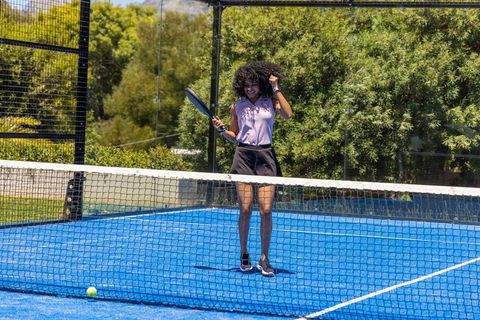 Young woman playing padel on bright blue court celebrating winning point with racket