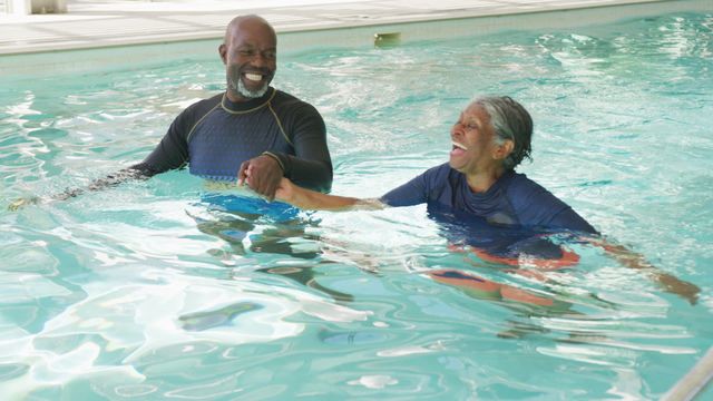 Senior African American couple swimming together in sunny pool, showcasing joyful retirement and active lifestyle. Perfect for promoting senior leisure activities, retirement communities, or healthy living for older adults.