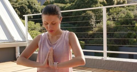 Rooftop woman meditating in pink tank top practicing mindfulness on sunny terrace wearing smartwatch