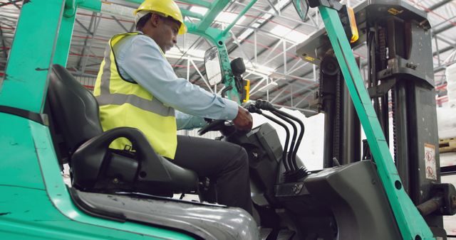 Professional forklift operator driving vehicle inside large warehouse. Person is wearing proper safety gear, including a helmet and high visibility vest, demonstrating commitment to workplace safety. Useful for illustrating themes related to industrial work, transportation logistics, job roles in warehouses, and workplace safety protocols.