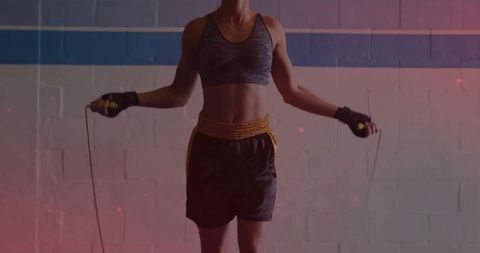 Female athlete jumping rope in moody garage gym with neon light and boxing wraps