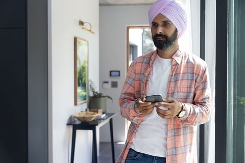 Man with Turban Holding Smartphone at Modern Home Entrance