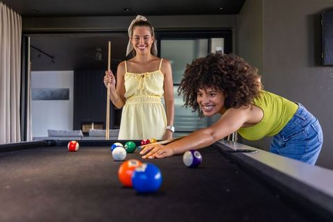Playing pool at home with friends, mixed-race women enjoying casual billiards night and laughter
