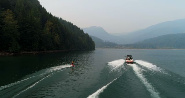 A person engages in waterskiing behind a speeding boat on a serene lake surrounded by forested mountains, with copy space. Waterskiing offers an exhilarating experience, blending high-speed aquatic adventure with the tranquility of natural landscapes.