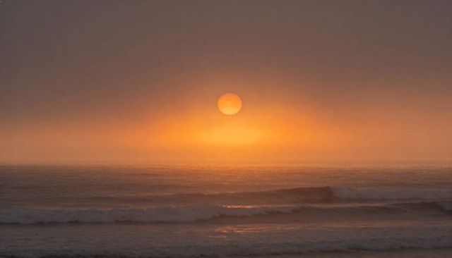 Golden sun rising over misty ocean waves casting warm reflection and halo at dawn