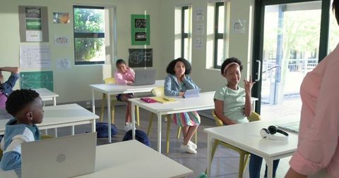 African American students raising hand and using laptops in sunlit modern classroom