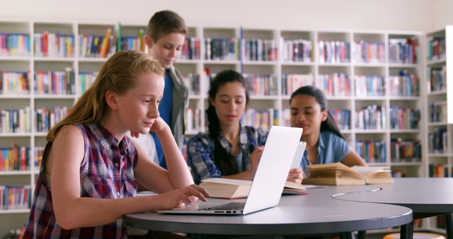 A group of diverse teenage students is engaged in studying together in a library, with a focus on collaboration and technology. Their concentrated expressions and the presence of books and a laptop suggest a productive learning environment.