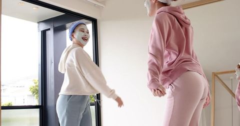 Diverse friends enjoying at-home skincare routine wearing facial masks and cozy hoodies