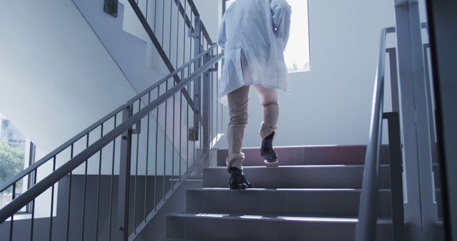 This image features a medical professional wearing a lab coat climbing stairs in a modern hospital. Ideal for use in healthcare and hospital-related articles, advertisements, brochures, and websites focusing on doctors, medical professionals, or healthcare environments. It highlights the busy and proactive nature of healthcare workers.