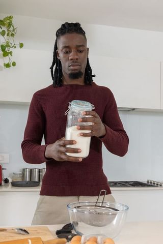 African american man holding jar of flour preparing to bake in home kitchen wearing maroon top