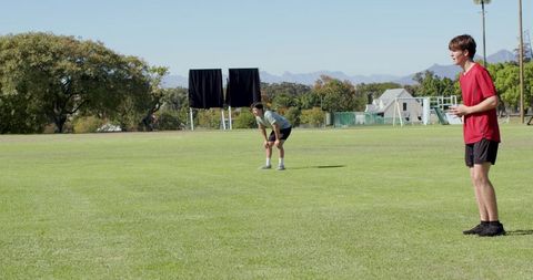 Teenager holding white ball standing on sideline during grass field sports practice